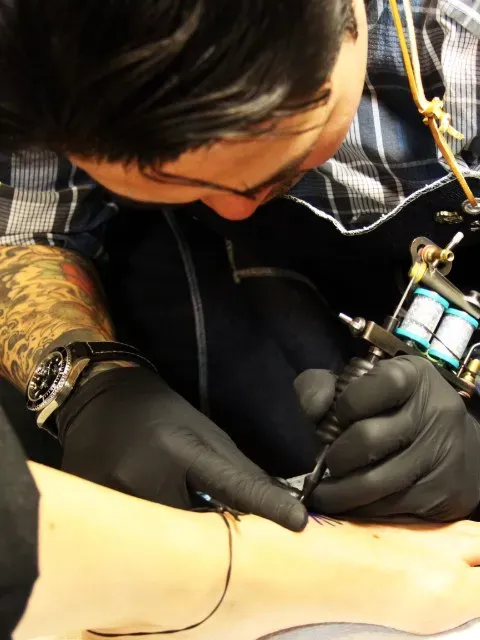 Tatuador trabajando con guantes y máquina de tatuar